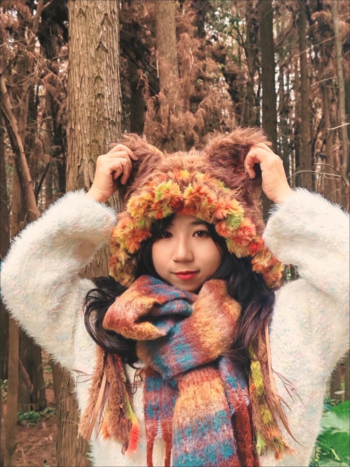 Customer photo wearing the brown animal-ear hat with colourful chenille flowers, outdoors with a knit scarf